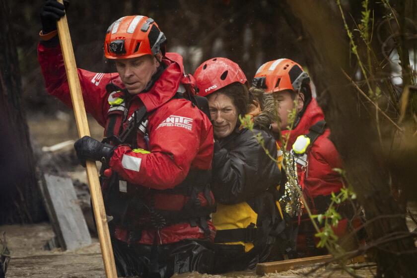 Firefighters rescue a woman from a homeless encampment that became surrounded by floodwater in the Santa Ana River during a rainstorm, Monday, Feb. 5, 2024, in San Bernardino, Calif. (AP Photo/Ethan Swope)