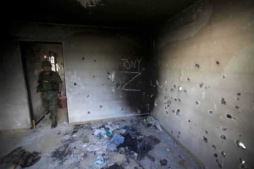 FILE - A soldier enters a bullet-riddled home covered by the initials of the Gulf Cartel (CDG) and Zetas (Z) in Ciudad Victoria, Tamaulipas state, Mexico, Sept. 6, 2014. (AP Photo/Eduardo Verdugo, File)