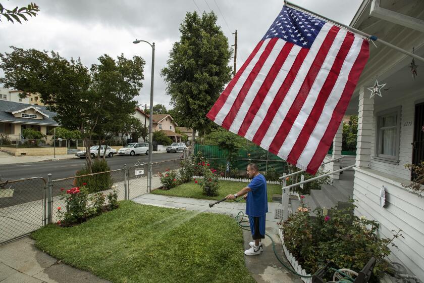 LINCOLN HEIGHTS, CA-MAY 20, 2022: Eddie Vasquez, 61, waters the front lawn of his home on Thomas St. in Lincoln Heights. Vasquez said that he waters the lawn once a week, giving it a good soaking. He has the American flag out in honor of the victims of 9/11 and also because of his nephew, who joined the Marines and is now Staff Sgt. Victor Martinez. It's going to be a summer of brown grass and hard choices for Southern California lawn owners facing the Metropolitan Water District's one day a week watering restrictions starting June 1. (Mel Melcon / Los Angeles Times)