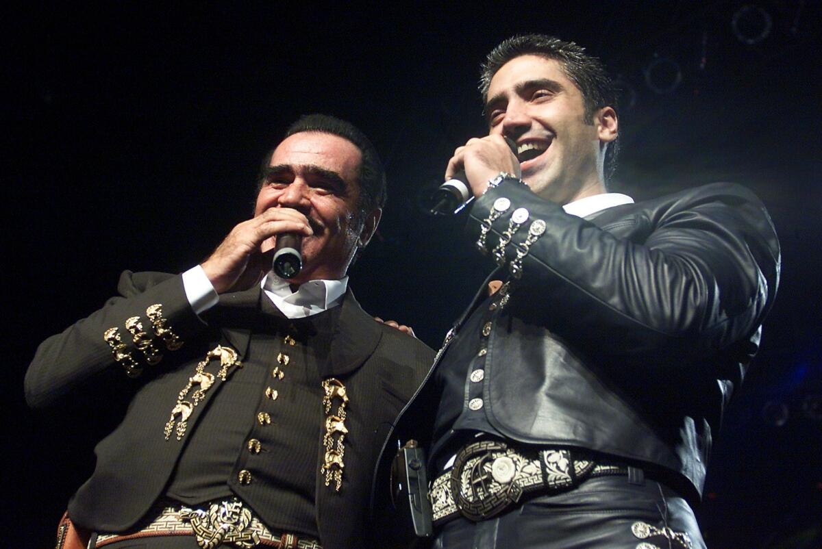 Vicente and Alejandro Fernández hold microphones as they sing onstage.