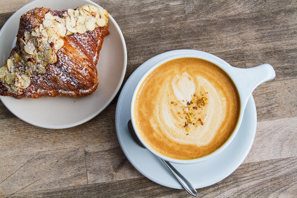 A latte with a foamy design sits beside a sweet croissant at Mandarin Coffee Stand 