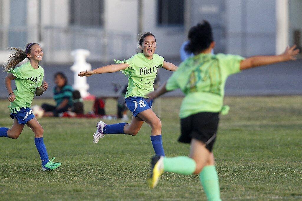 Newport Coast's Monique Martin, center, celebrates with teammates Sophia Rhee, right, and Paris Ammari, left, after Martin scored a goal during a Pilot Cup girls' 5-6 silver division game against Whittier on Thursday.