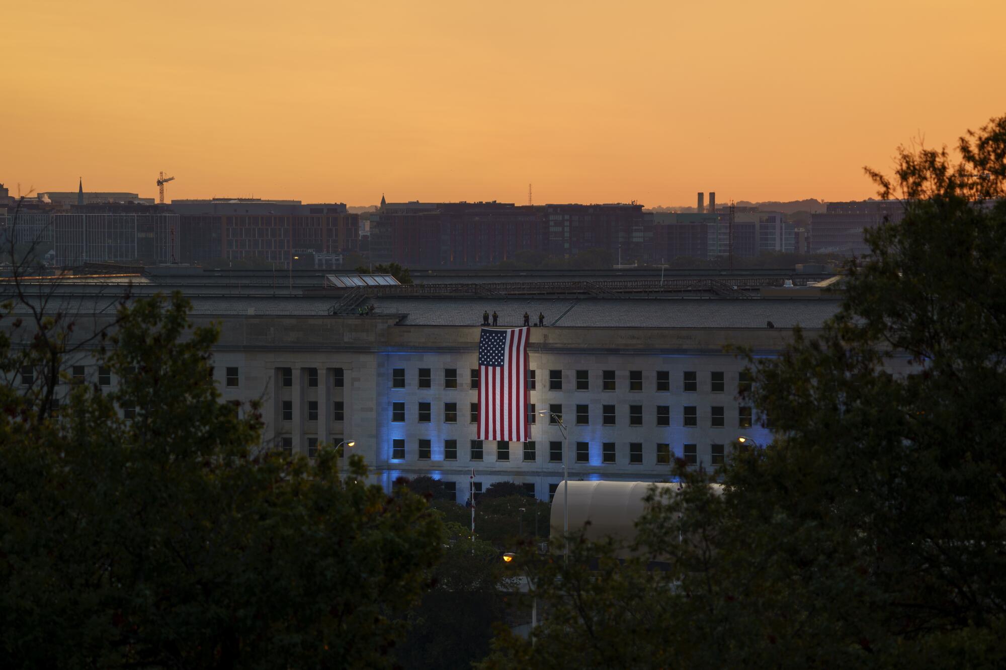 An American flag is unfurled from the roof of the Pentagon at sunrise. 