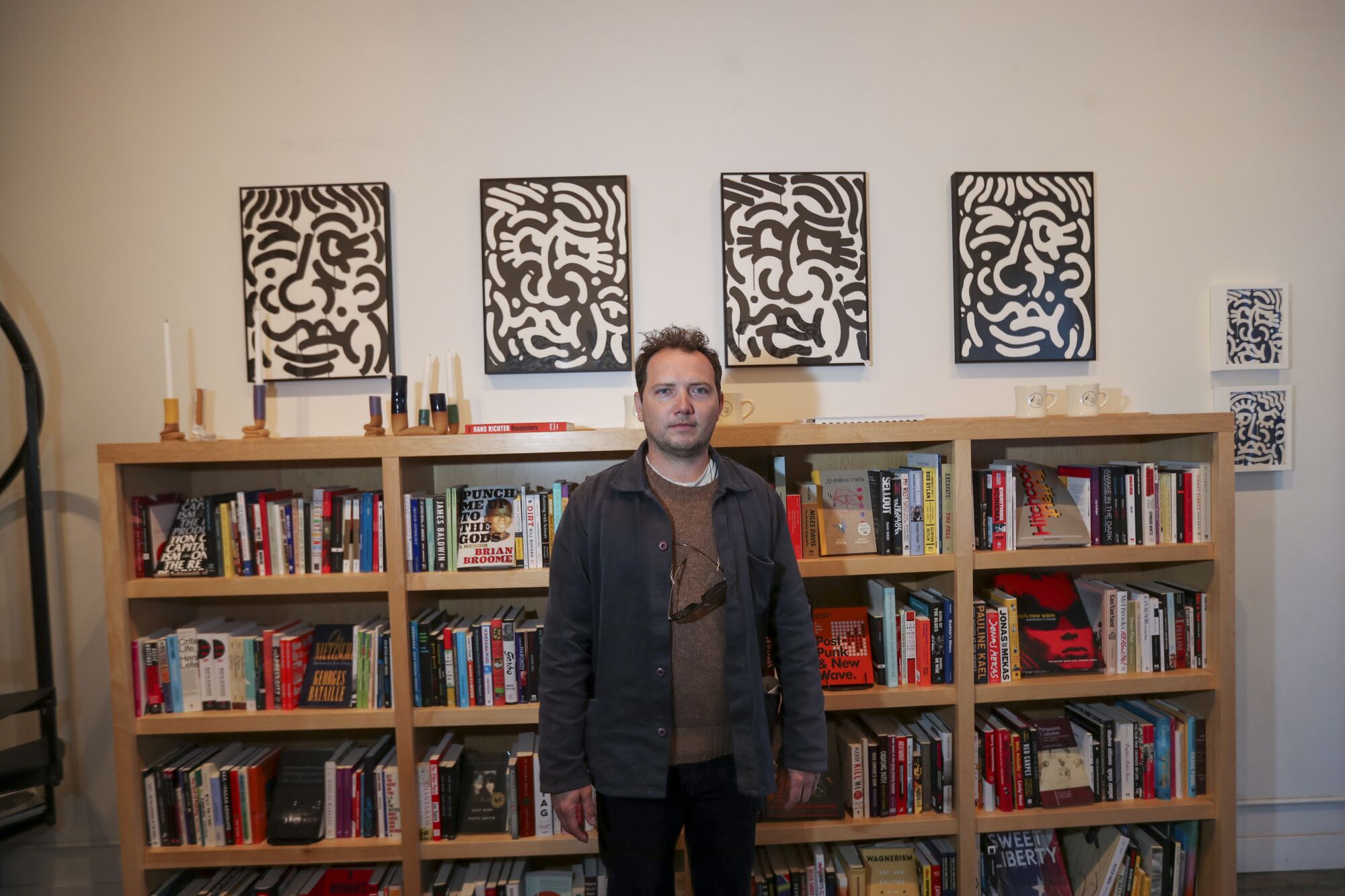 A man standing in front of bookcases and black-and-white artwork on the wall.