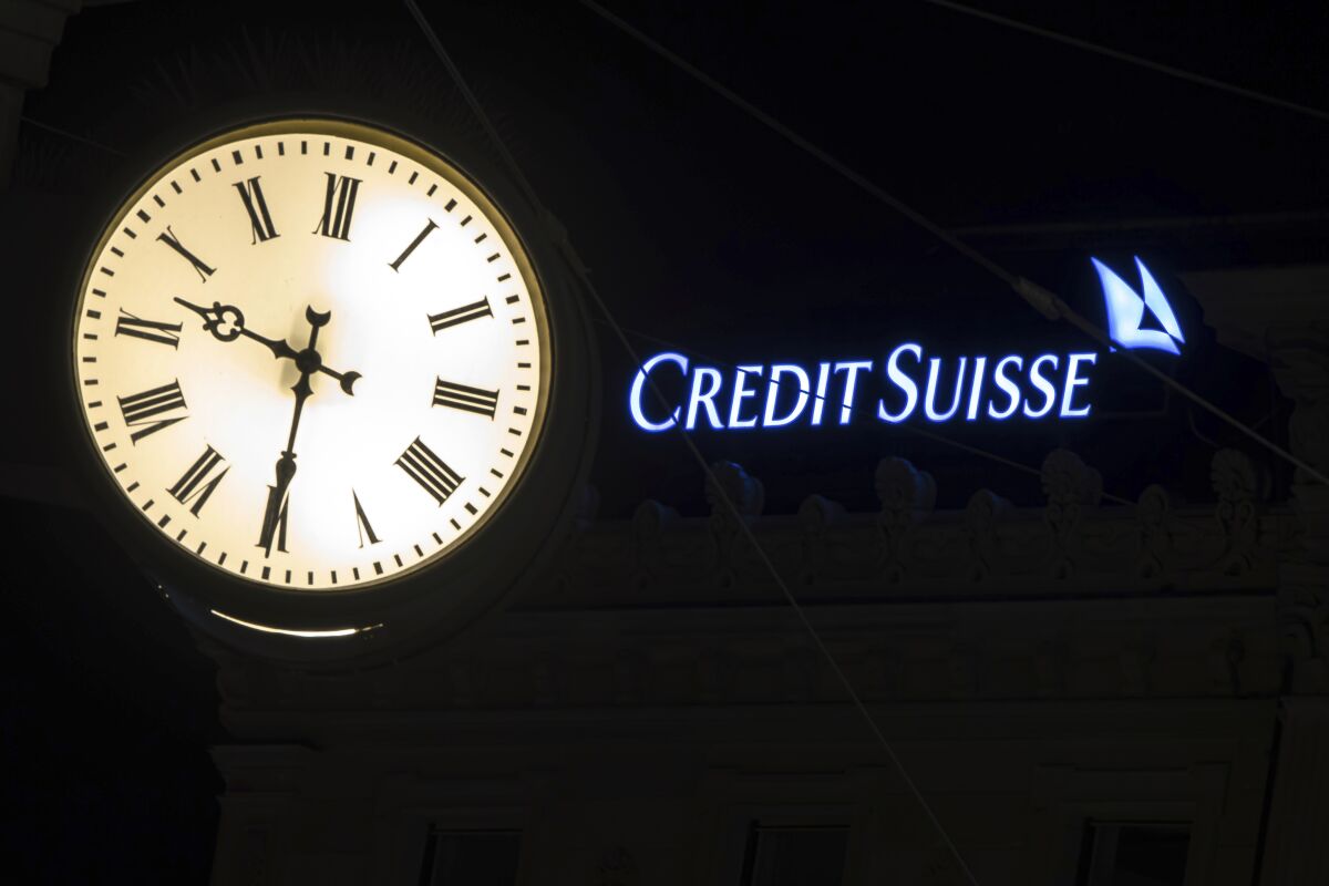 The illuminated logo of Swiss bank Credit Suisse is seen behind a clock at the banks headquarters at Paradeplatz in Zurich, Switzerland on Saturday, March 18, 2023. (Michael Buholzer/Keystone via AP)