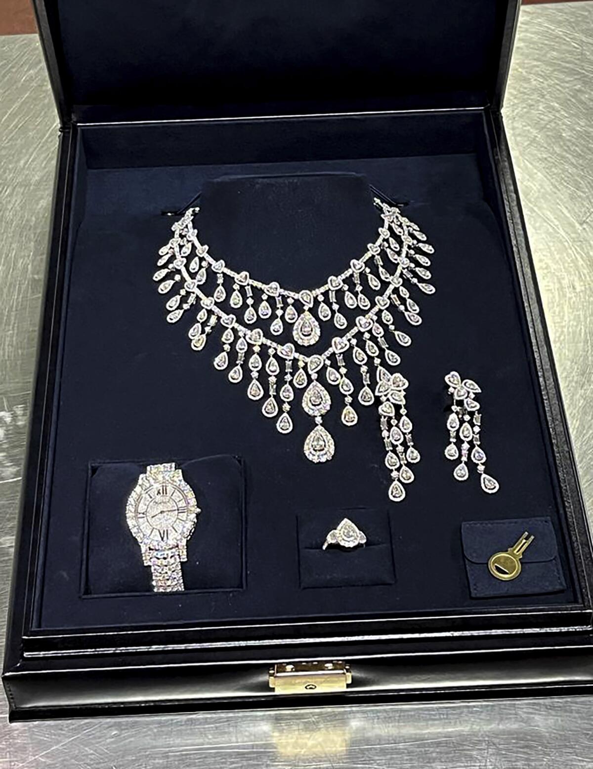 A case holds an ornate diamond necklace, earrings, ring and watch. 