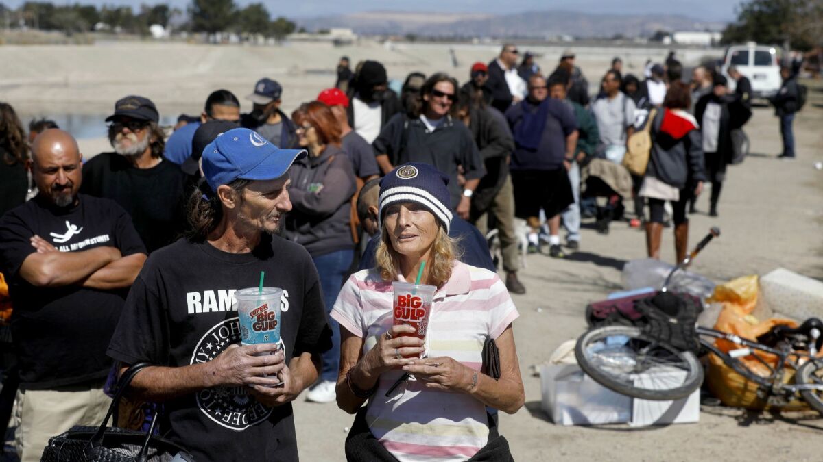 Mark Randall, 47, left, and his wife, Tonya Randall, 61, wait in line with others in February for a 30-day motel voucher from the Orange County Health Care Agency at the homeless encampment along the Santa Ana River in Anaheim.
