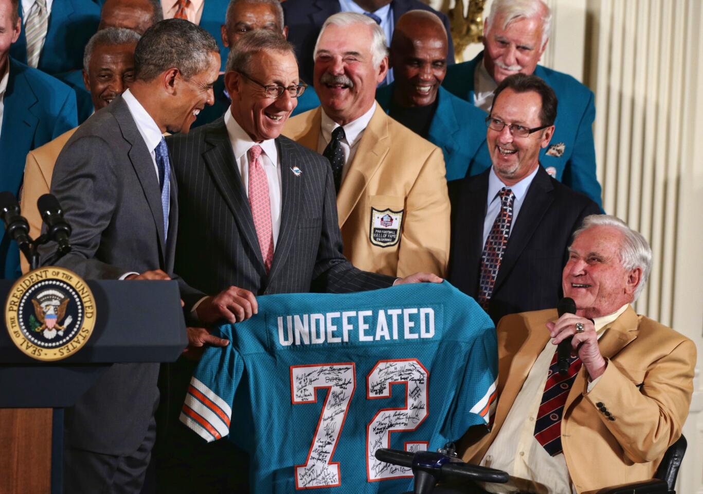 U.S. President Barack Obama (L) is presented with a jersey by current team owner Stephen Ross (2nd L) as members of the 1972 Miami Dolphins, head coach Don Shula (R), running back Larry Csonka (3rd L) and other members look on during an East Room event August 20, 2013 at the White House in Washington, DC. President Obama hosted the undefeated 1972 Super Bowl champions who didn't get the chance to be honored at the White House back then.