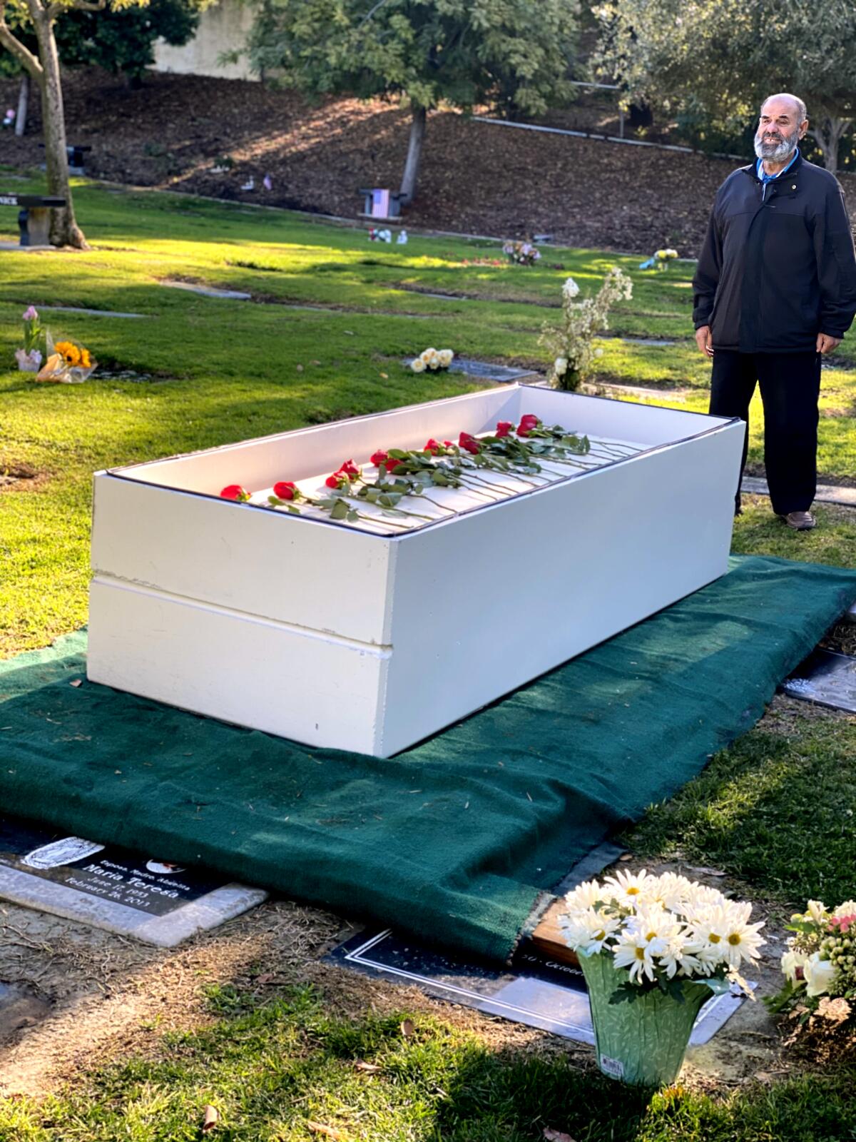 A man stands over a coffin at a graveyard 