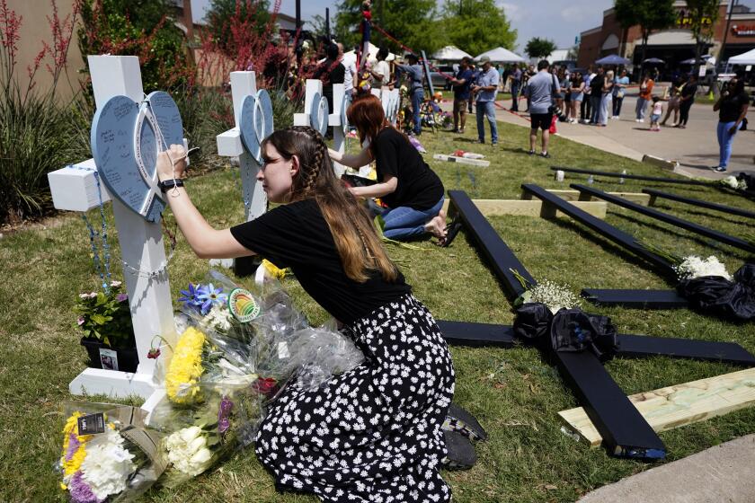 Jennifer Seeley signs a cross that stands by others at a makeshift memorial by the mall where several people were killed several days earlier, Monday, May 8, 2023, in Allen, Texas. Seeley, an employee at the Crocs store at the mall, said she was signing the cross for one of the victims, an acquaintance who worked as a security guard at the mall. (AP Photo/Tony Gutierrez)