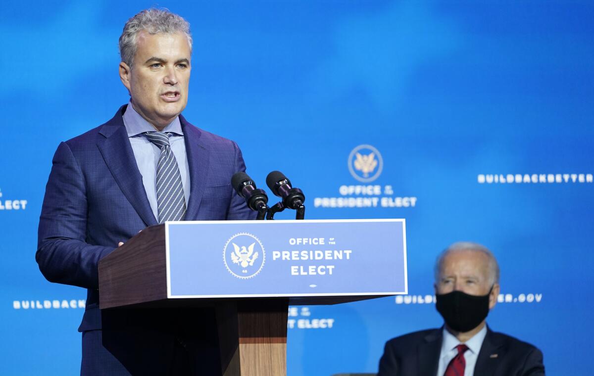 Jeff Zients speaks at a lectern as then-President-elect Joe Biden listens.