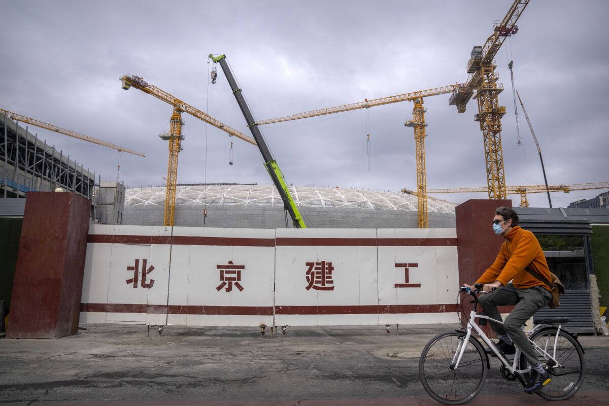 A man wearing a face mask rides a bicycle past a construction site in Beijing, Thursday, May 12, 2022. China's leaders are struggling to reverse a deepening economic slump while keeping a "zero-COVID" strategy that has shut down Shanghai and other cities. (AP Photo/Mark Schiefelbein)