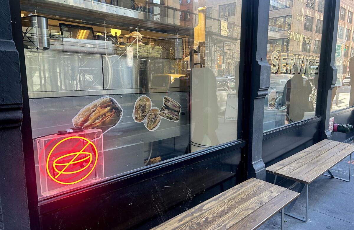 A neon sign in the window of a sandwich shop depicts a bowl inside a circle with a line over it.