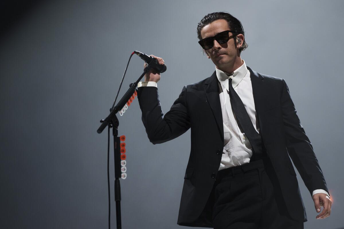 Matty Healy prepares to sing into a mic while wearing sunglasses, a black suit and tie and a white shirt 