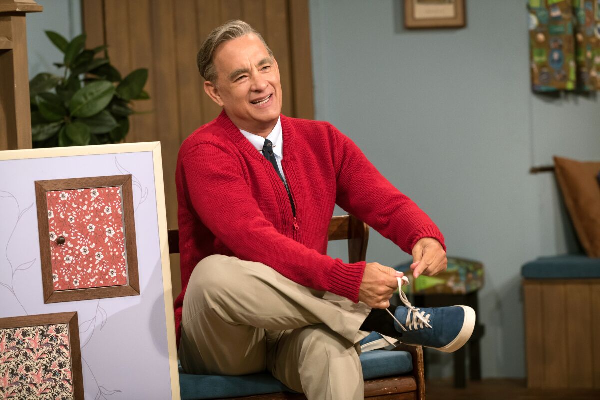 A smiling man in a red sweater ties his shoe in the movie "A Beautiful Day in the Neighborhood."
