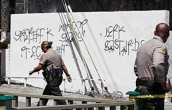 Los Angeles County sheriff's deputies walk near freshly painted graffitti in a South Los Angeles alley where several people, including Rashaun Williams, 29, were injured in a drive-by shooting July 11 as people gathered to mourn the death of Woodrow Player Jr., who had been shot and killed by officers the day before.