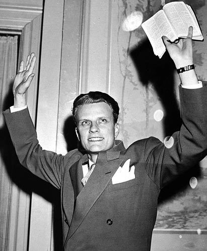 Evangelist Billy Graham holds a Bible aloft in the mid-1950s.