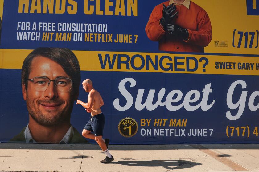 Los Angeles, CA - June 04: A man jogs by the new Netflix movie Hit Man wall poster on Beverly Blvd and Edinburgh Ave on Tuesday, June 4, 2024 in Los Angeles, CA. (Michael Blackshire / Los Angeles Times)