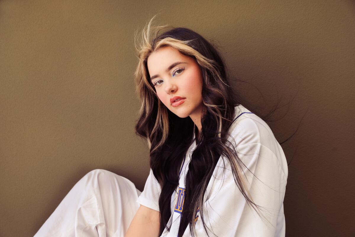 A young female singer in a white T-shirt and white trousers poses for a portrait