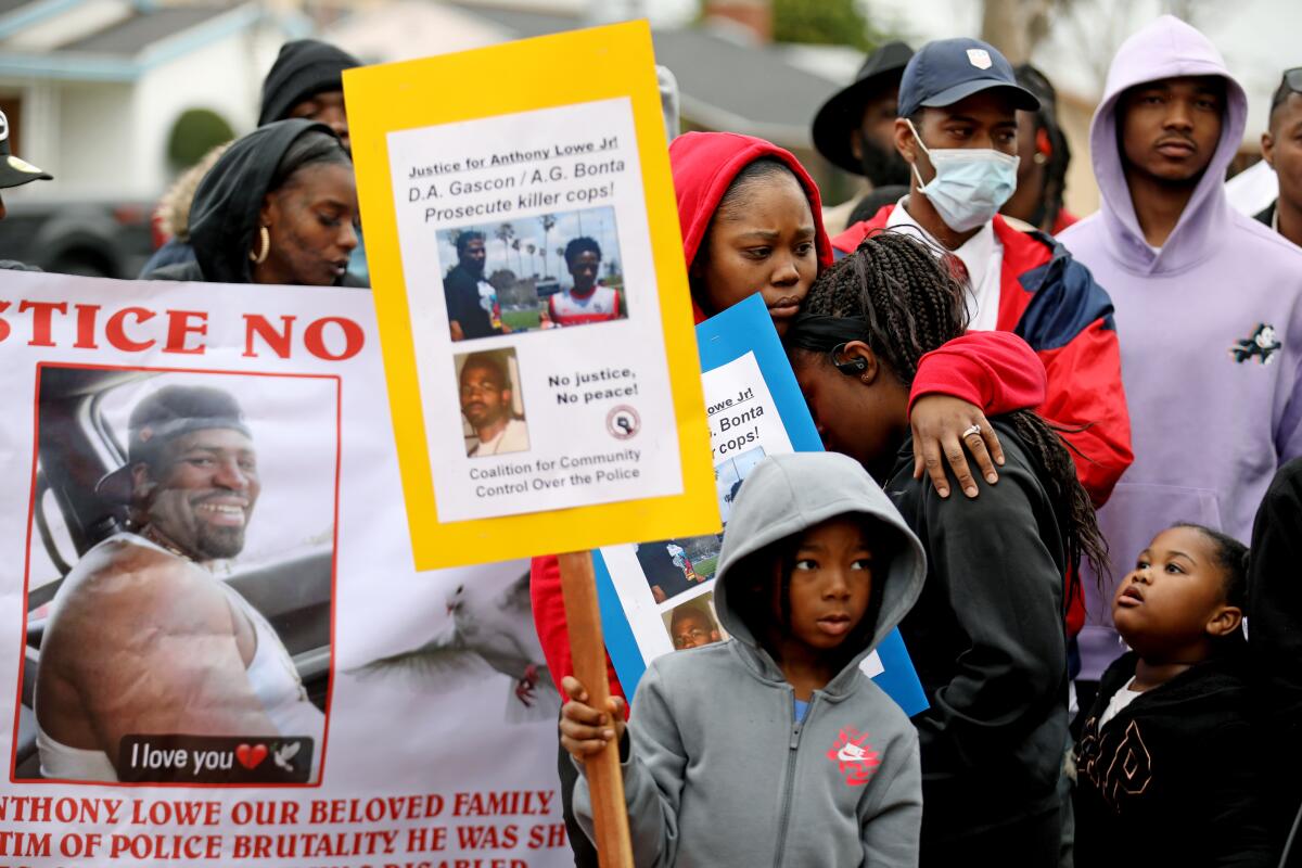 Children and adults stand together holding placards; some hug.