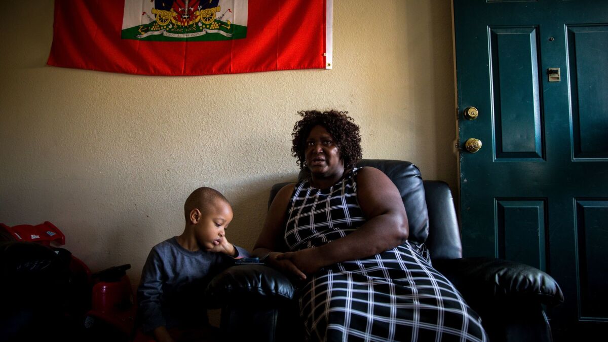 Beneath a Haitian flag, Joshua Valsaint, 4, watches a children's show on a phone while his mother, Haitian immigrant Josiane Valsaint, discusses her temporary protective status in the United States.