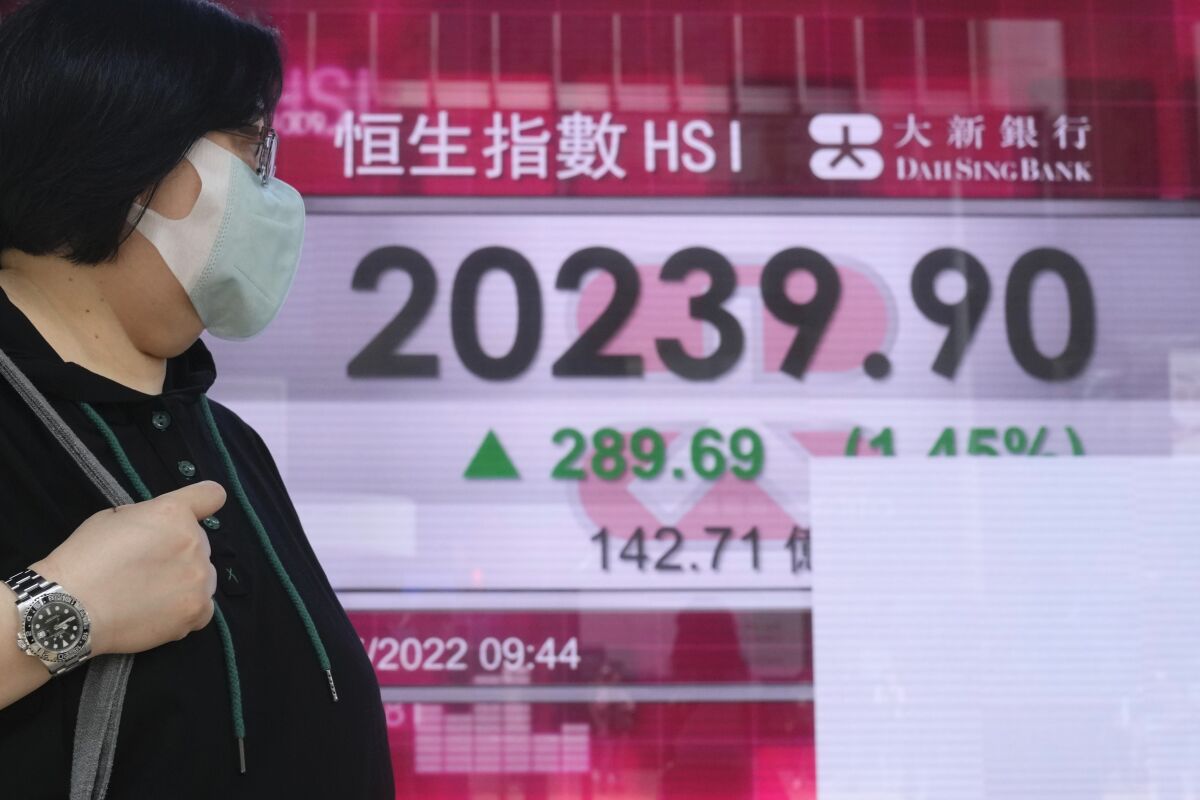A woman wearing a face mask walks past a bank's electronic board showing the Hong Kong share index in Hong Kong, Tuesday, May 17, 2022. Shares advanced in Asia on Tuesday after another wobbly day on Wall Street extended a losing streak for markets. (AP Photo/Kin Cheung)