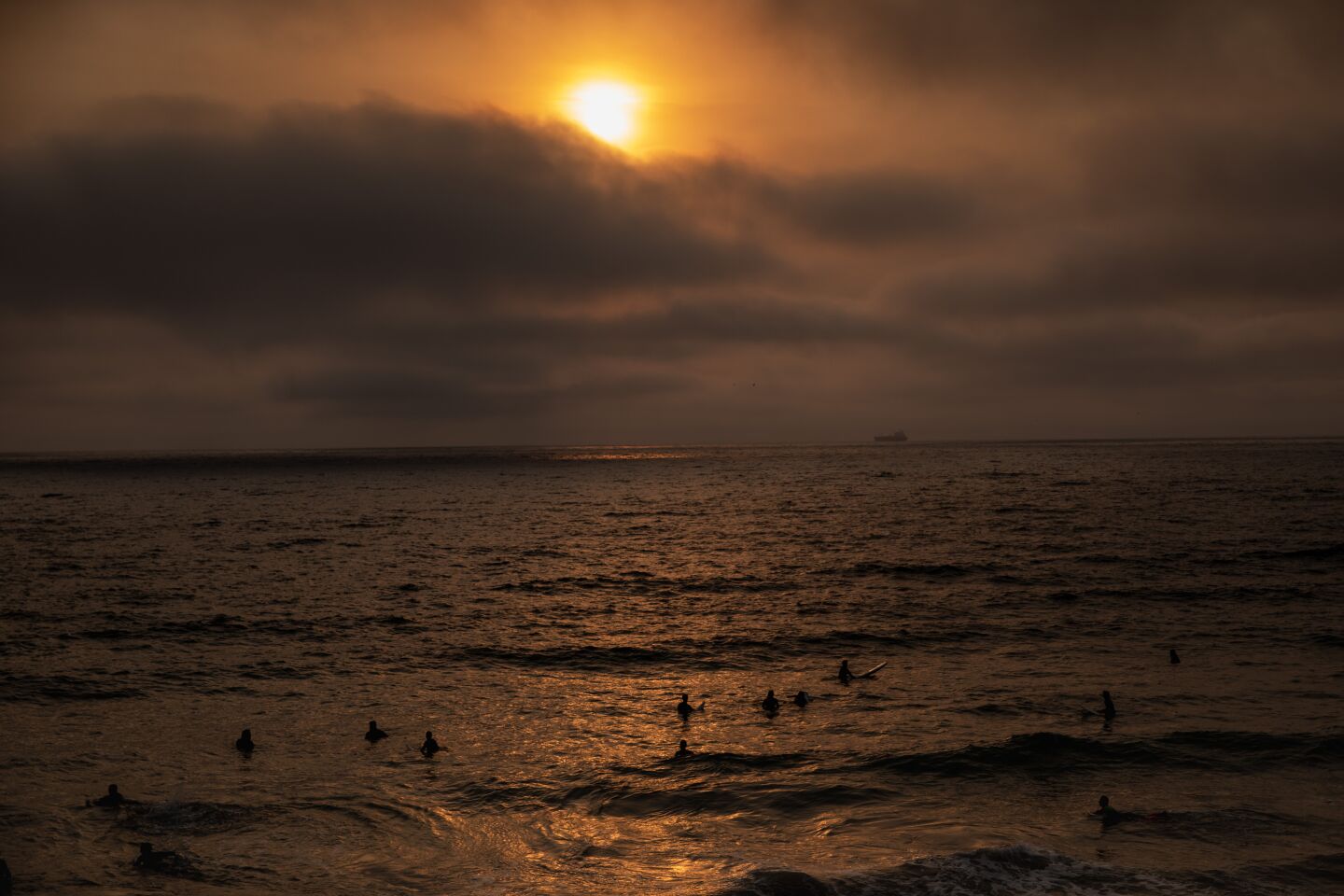 Surfers near the Manhattan Beach Pier under a smoky sunset.