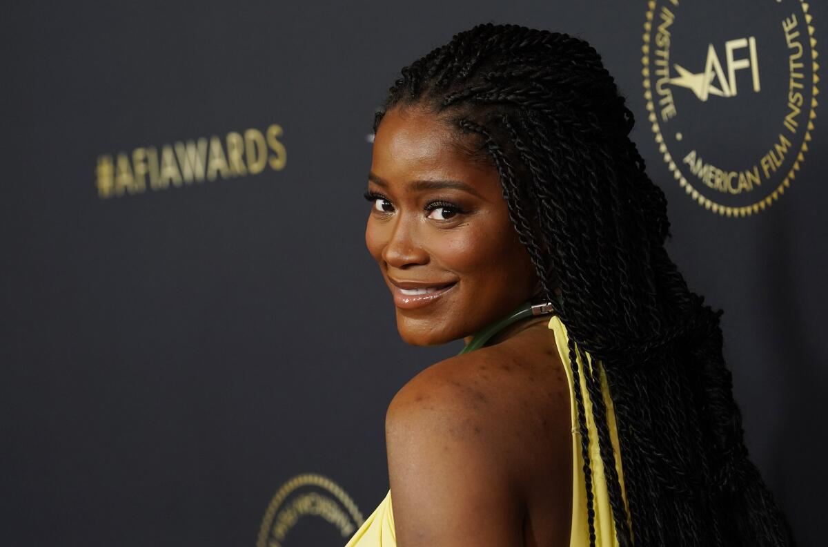 Keke Palmer smiling over her shoulder while wearing a yellow dress