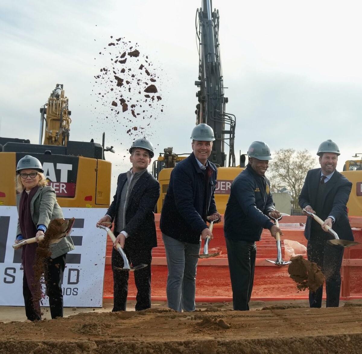 A line of five people with shovels, breaking ground at a construction site