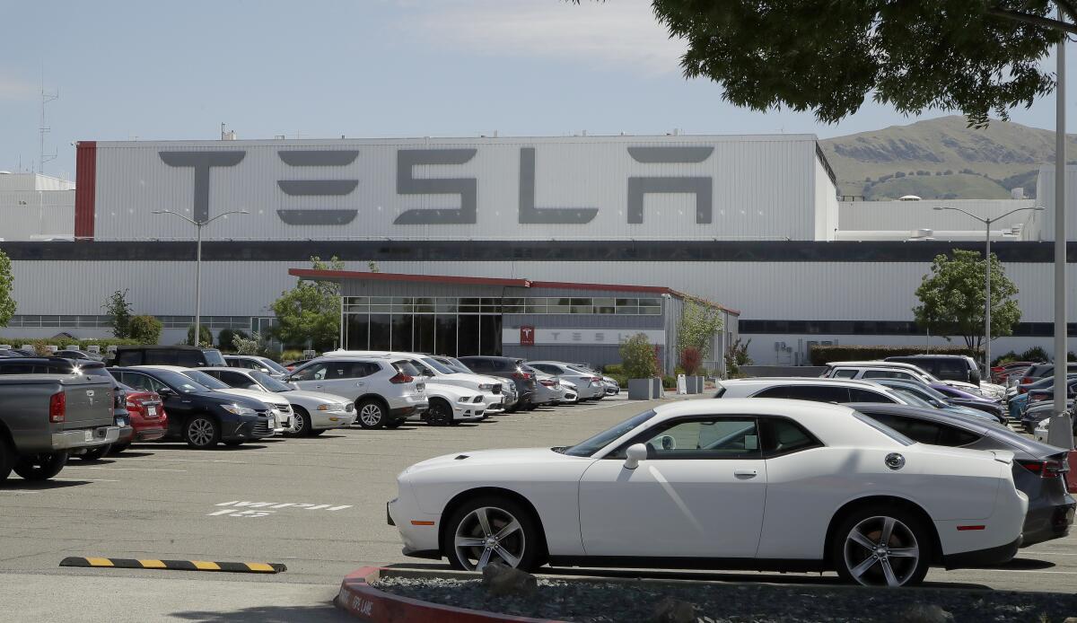 Cars in a parking lot outside a large Tesla factory building