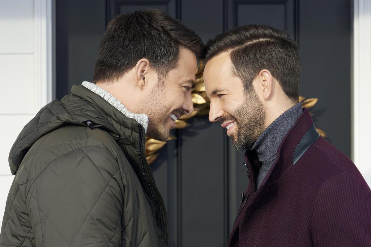 Two men stand in front of a door, smiling with their foreheads pressed together.