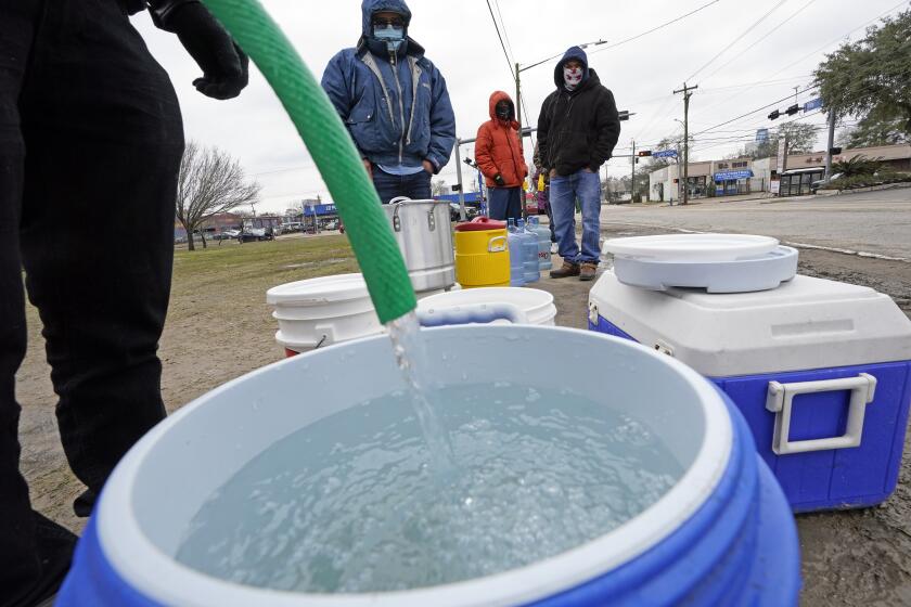 A water bucket is filled as others wait in near freezing temperatures to use a hose from public park spigot Thursday, Feb. 18, 2021, in Houston. Houston and several surrounding cities are under a boil water notice as many residents are still without running water in their homes. (AP Photo/David J. Phillip)