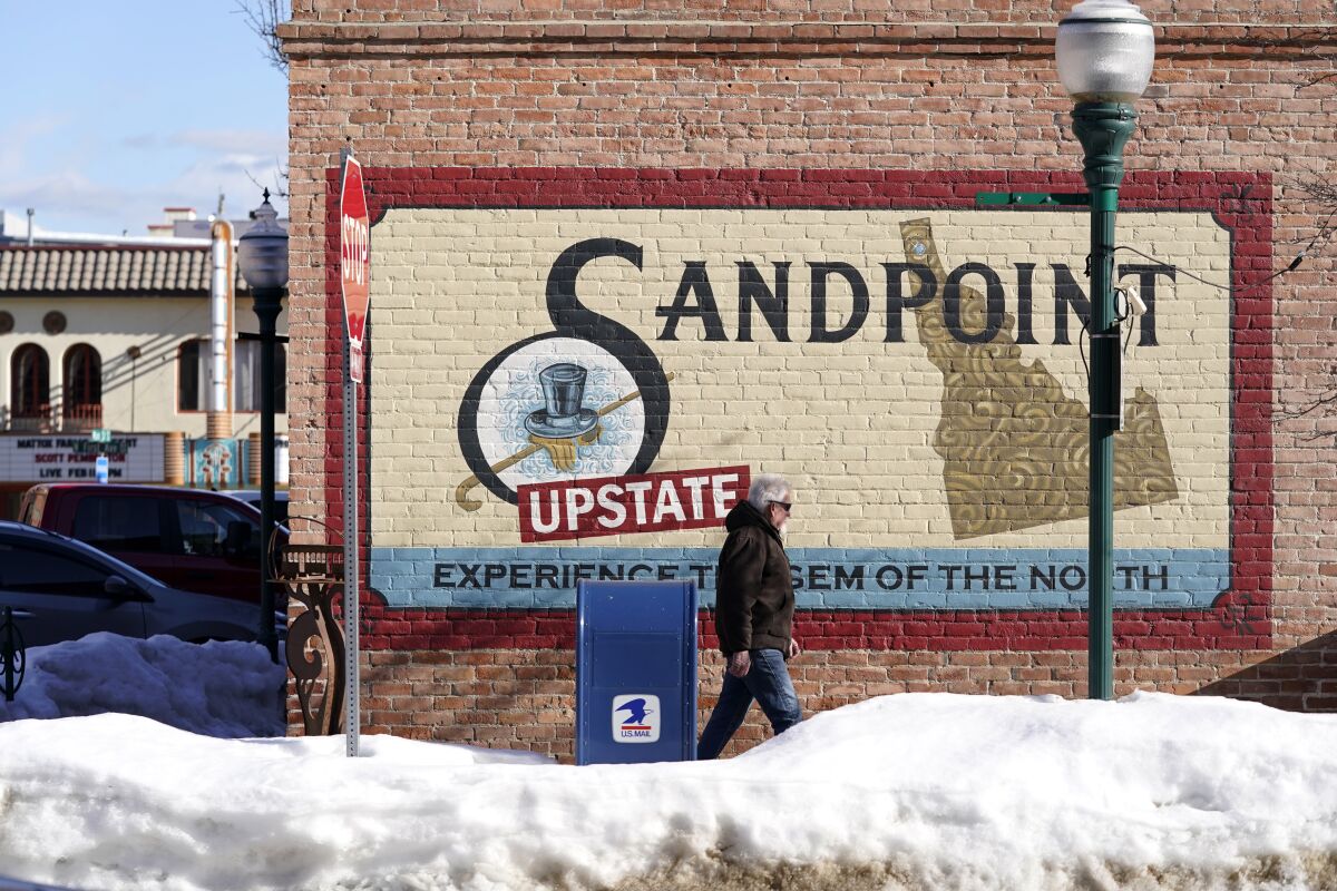 A pedestrian walks past a mural, Monday, Feb. 7, 2022, in downtown Sandpoint, Idaho. The Mayor of Sandpoint and many residents worry that the trend of a growing number of real estate companies advertising to conservatives that they can help people move out of liberal bastions like Seattle and San Francisco and find homes in places like rural Idaho is not good for their community. (AP Photo/Ted S. Warren)