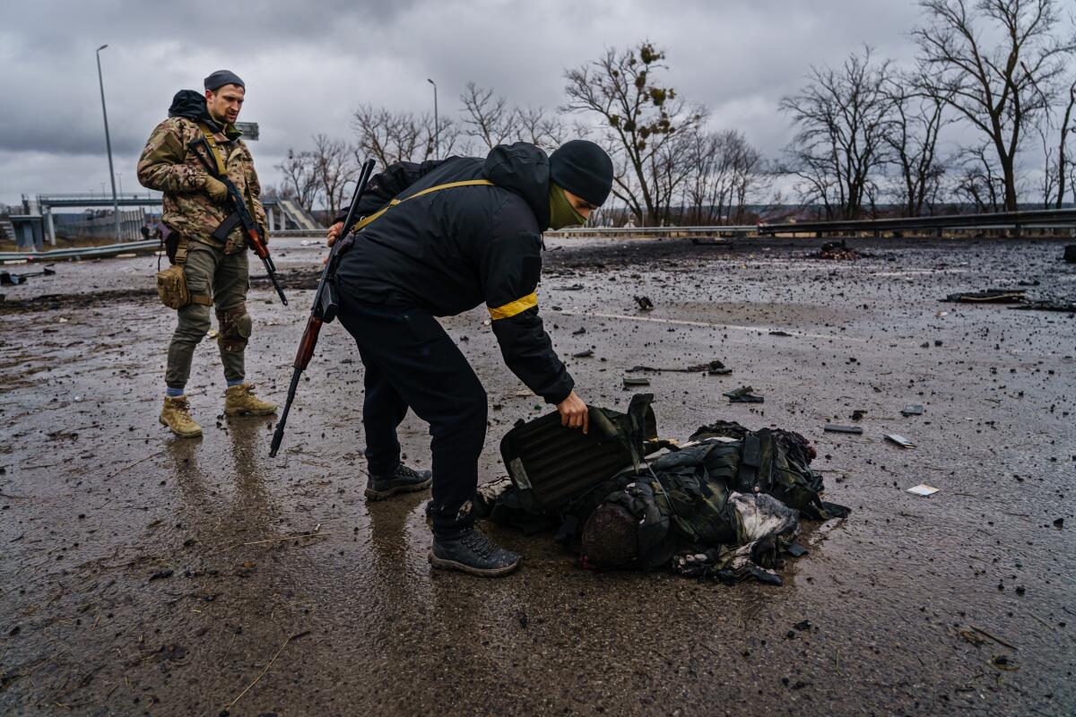 Ukrainian soldiers salvage equipment off a body of a dead Russian soldier.