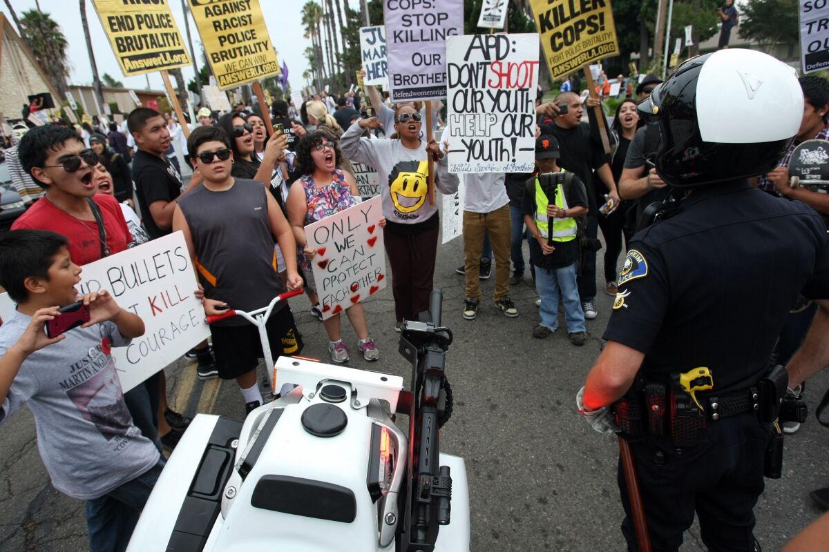 An Anaheim police officer observes as residents in Anaheim protest after fatal police shootings last summer.