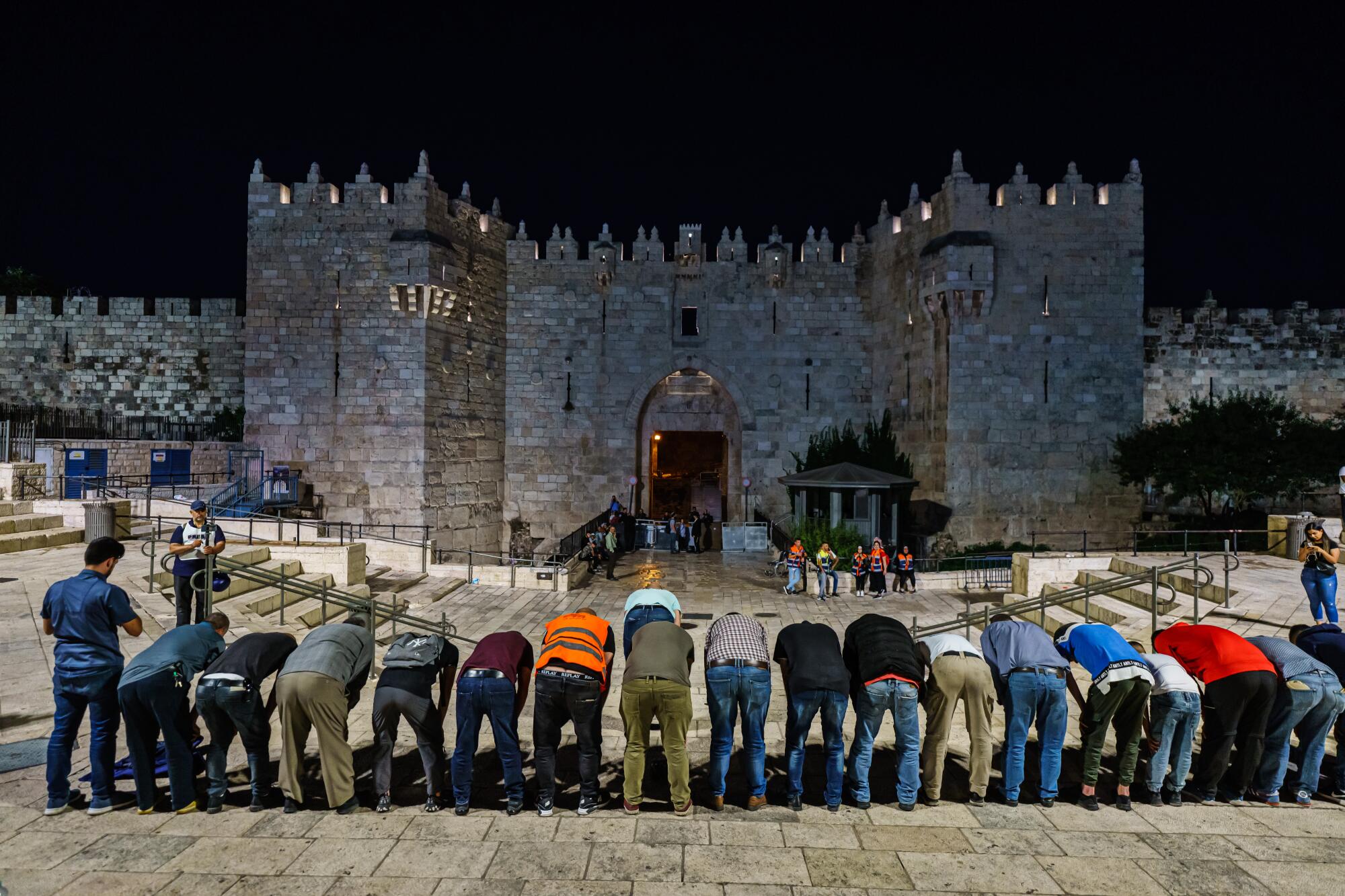 Seen from the back, a line of men behind at the waist in front of a stone gateway.