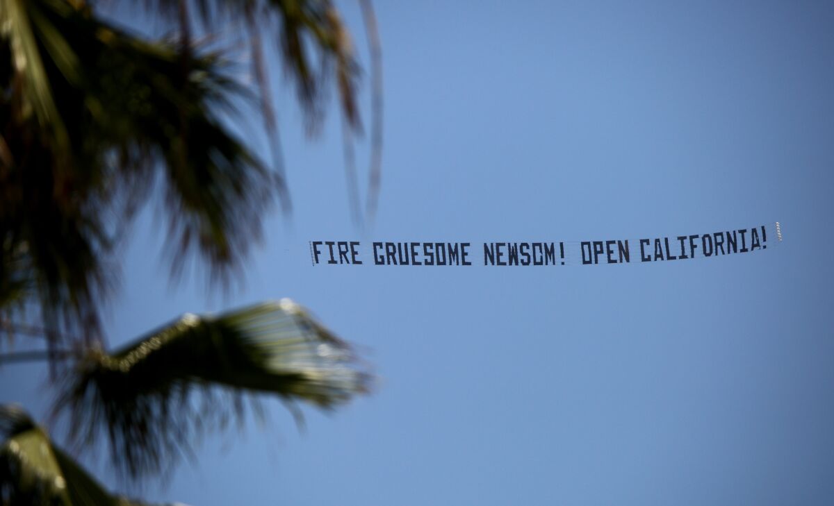 A small airplane flies a sign that reads "FIRE GRUESOME NEWSOM! OPEN CALIFORNIA!" during a protest over Huntington Beach on Friday.