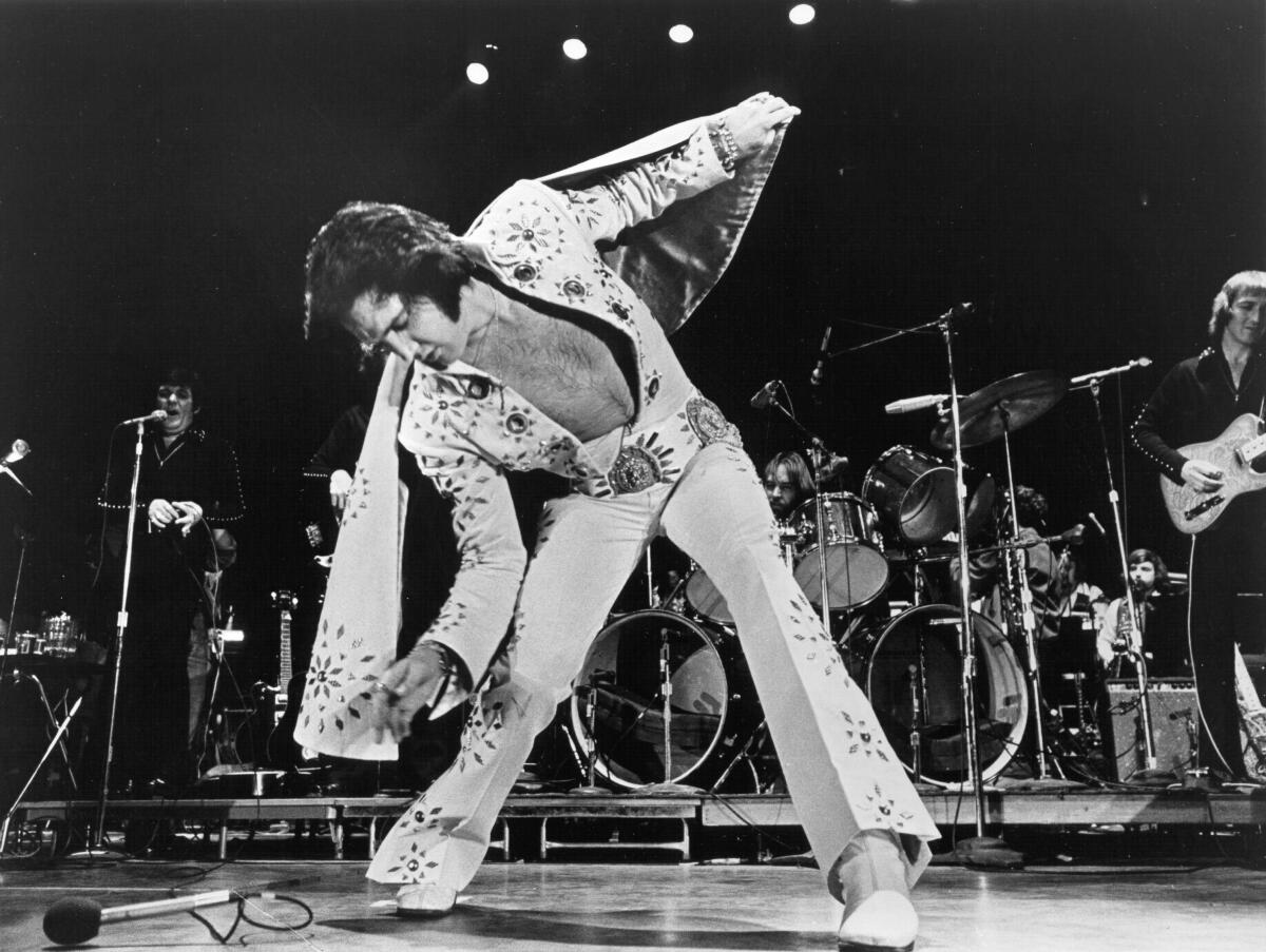 A singer in a white jumpsuit performs onstage. 