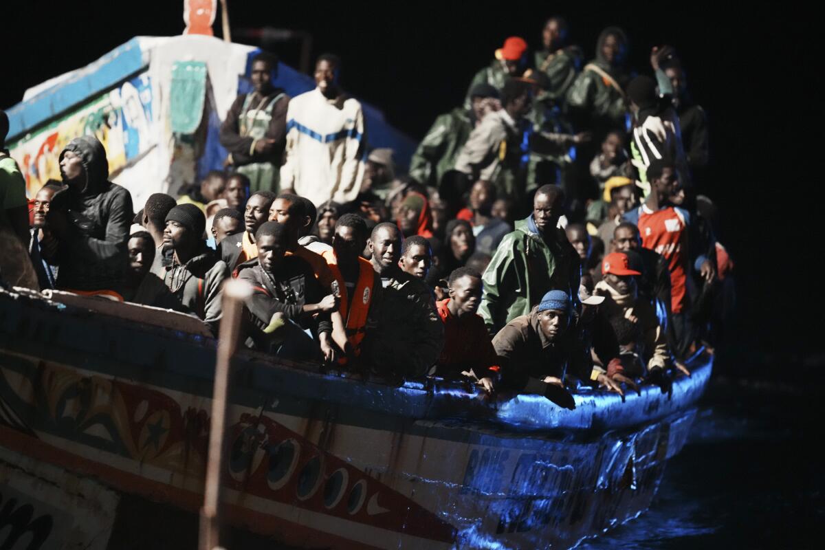 Migrants crowd a wooden boat in the water.