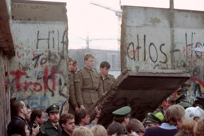 East German border guards look through a gap in the Berlin Wall.