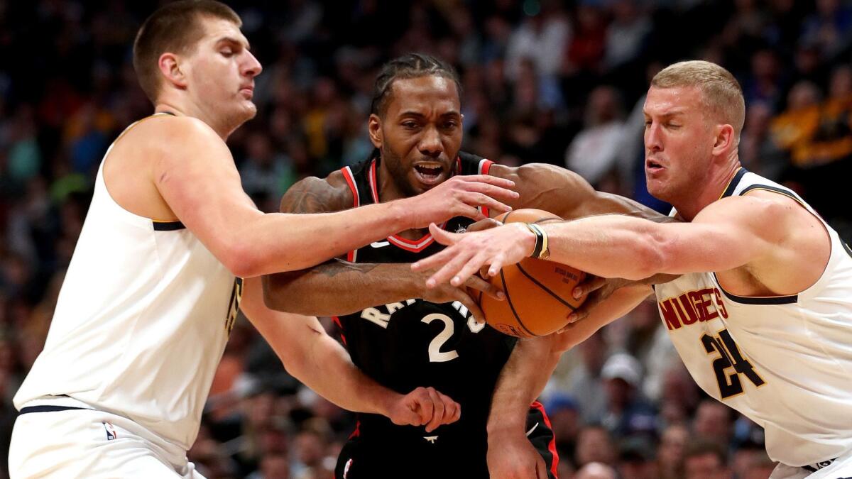 Nuggets big men Nikola Jokic, left, and Mason Plumlee, right try to stop a drive by Raptors forward Kawhi Leonard on Sunday.