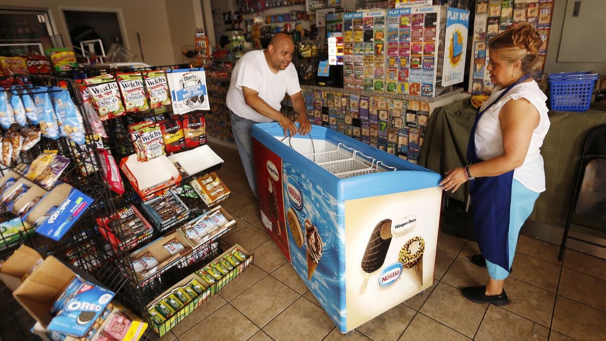 Carlos Zuniga, with mother Martha Hernandez, cleans out an ice cream freezer at Zuniga's Market in Koreatown. He threw out roughly $1,000 in milk, popsicles and ice cream after the power went out Friday at his shop.