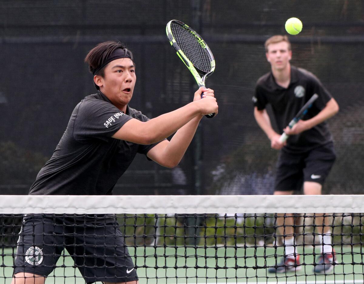 Sage Hill School doubles player Alan Wang returns the ball as Matthew Strok looks on in the background against Beckman in the CIF Southern Section Division 1 championship match at the Claremont Club on Friday.