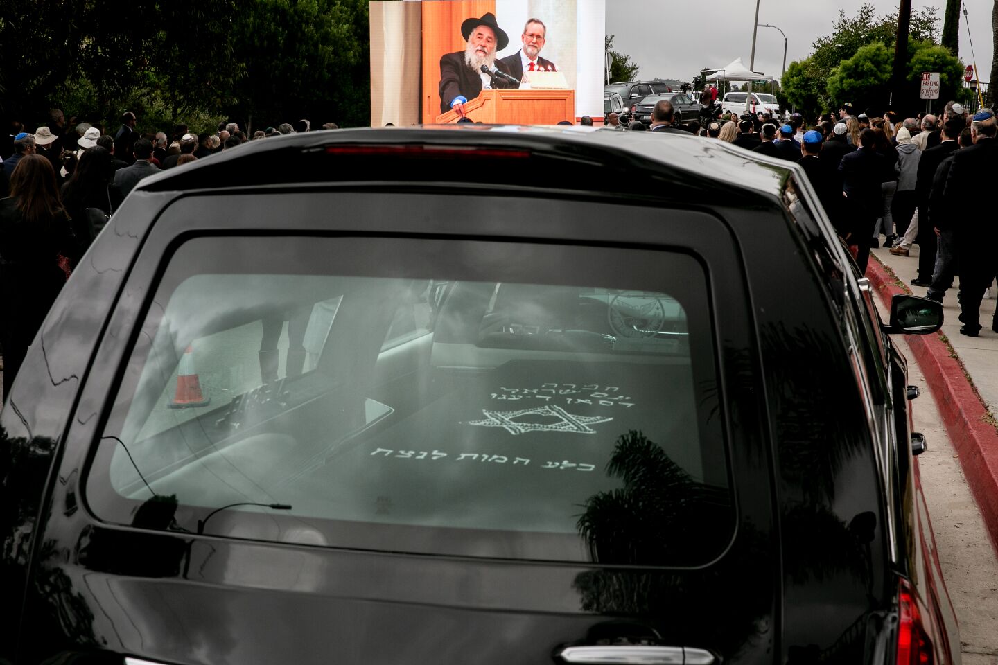 Rabbi Yisroel Goldstein is seen on a screen to an overflow crowd of mourners gather outside of Chabad of Poway for a memorial service for Lori Gilbert Kaye on April 29, 2019 in Poway, California. Kaye was killed on Saturday when a gunman opened fire inside the synagogue.