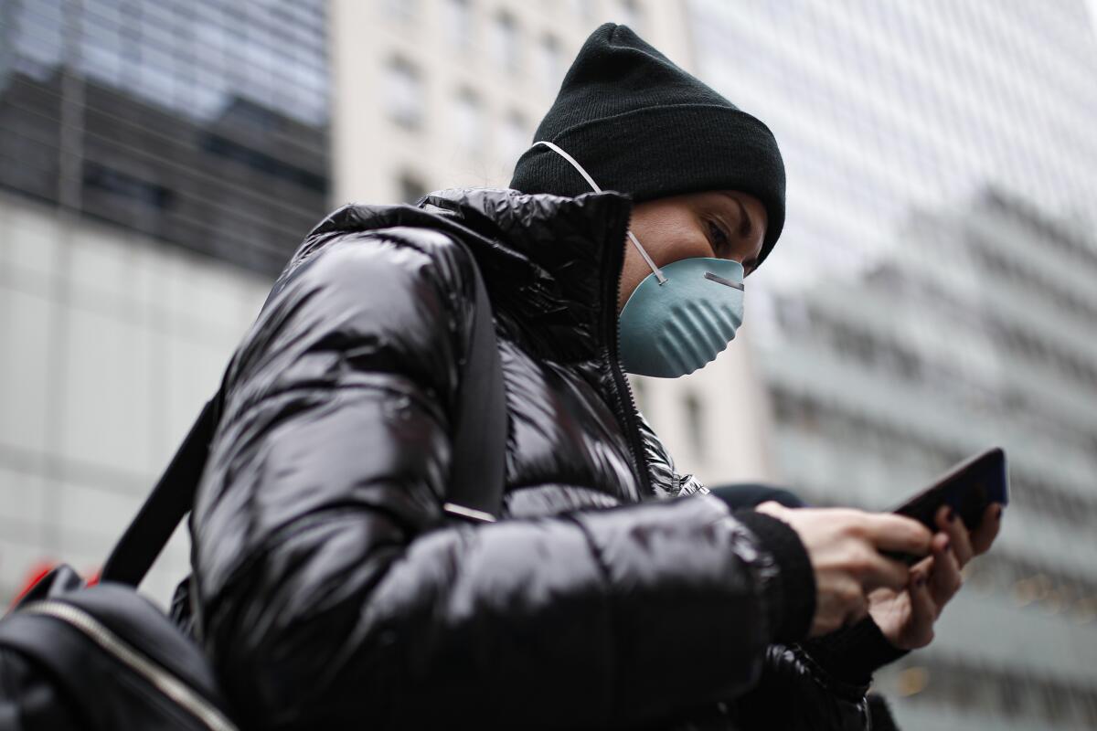 Una persona usa su teléfono celular, y también su máscara, para protegerse del coronavirus en Nueva York el 12 de marzo del 2020. (AP Photo/John Minchillo)