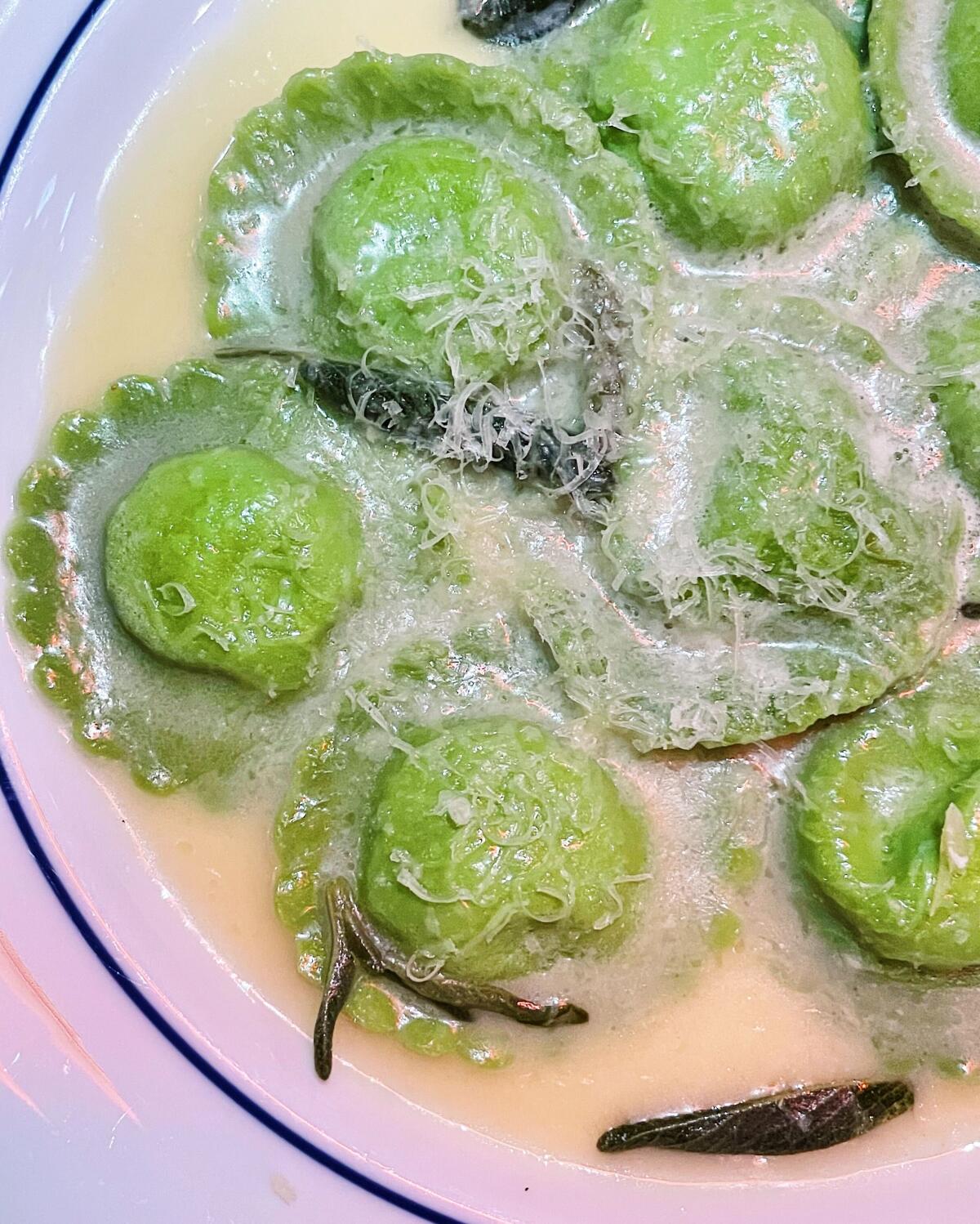 A plate of round green ravioli in butter sauce with shredded cheese