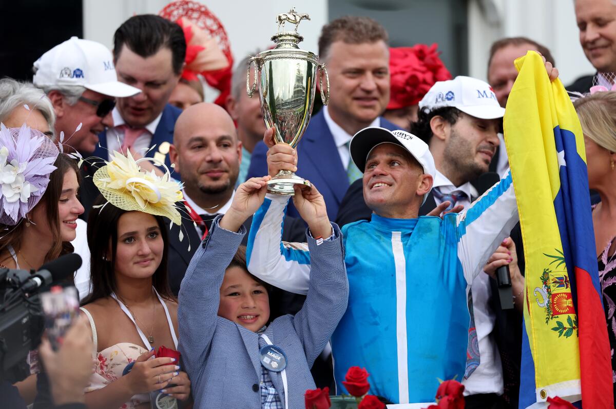 Javier Castellano hoists the Kentucky Derby trophy in one hand and the the flag of Venezuela in the other