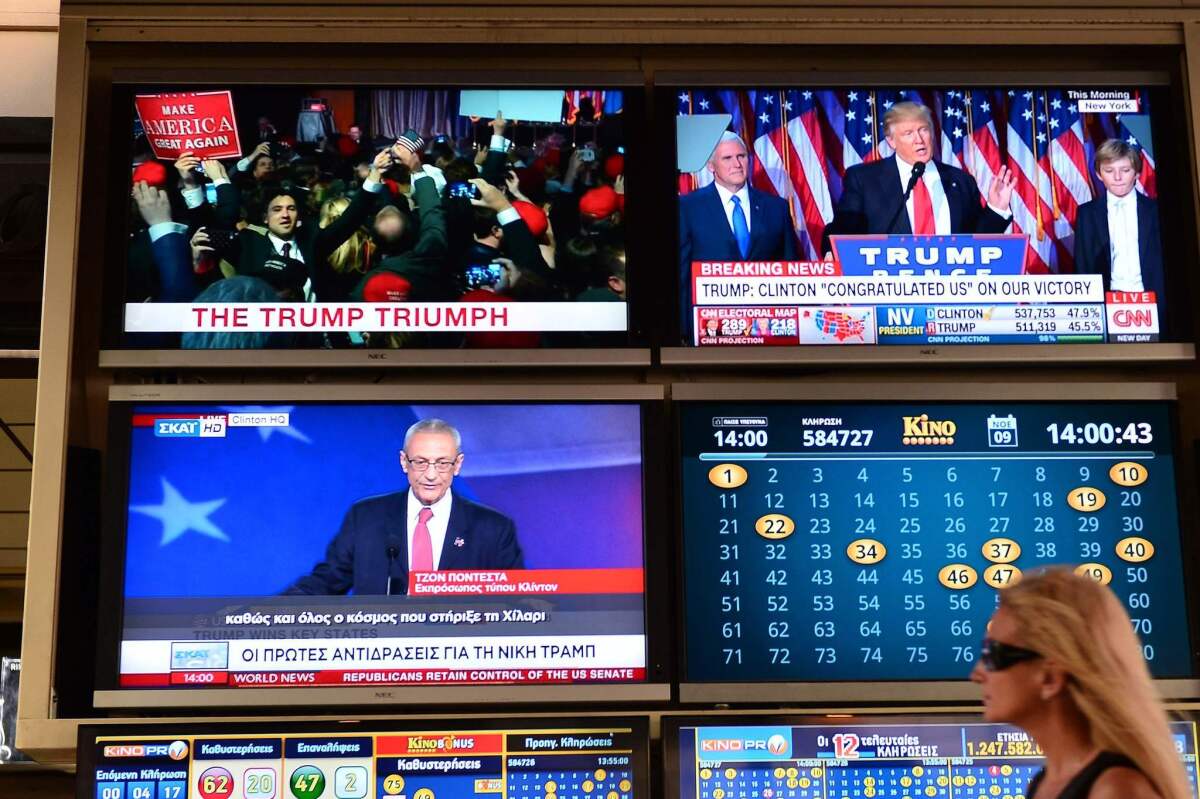 A woman walks past TV monitors displaying results of the U.S. presidential elections at an outdoor cafe in Athens on Nov. 9.