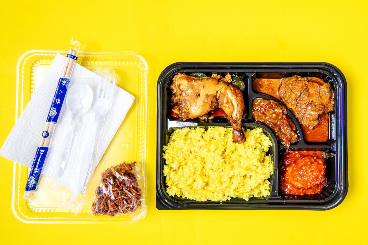 A plastic to-go tray filled with chicken and side dishes, with chopsticks