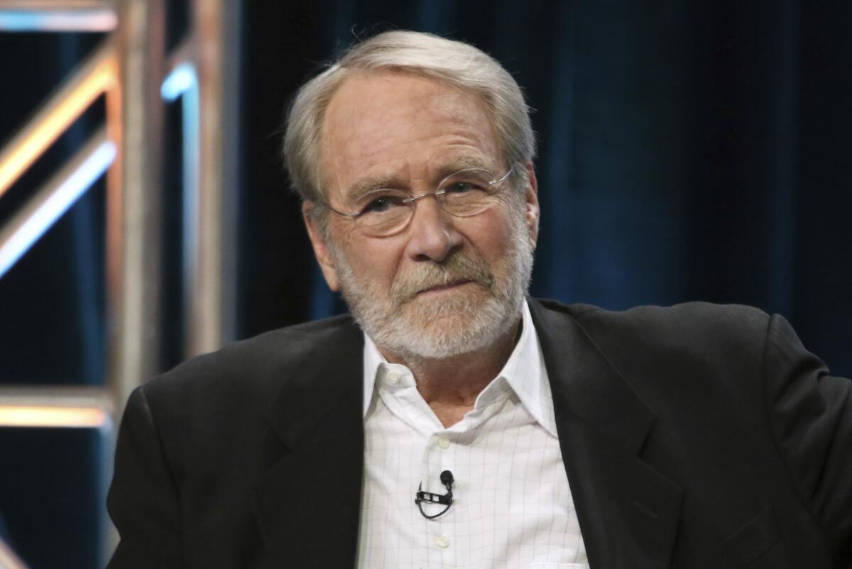 Martin Mull wears a dark blazer, glasses and lavalier mic attached to a white button-up at a panel discussion